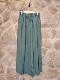 Green pants hanging on a wooden hanger against a stone wall.