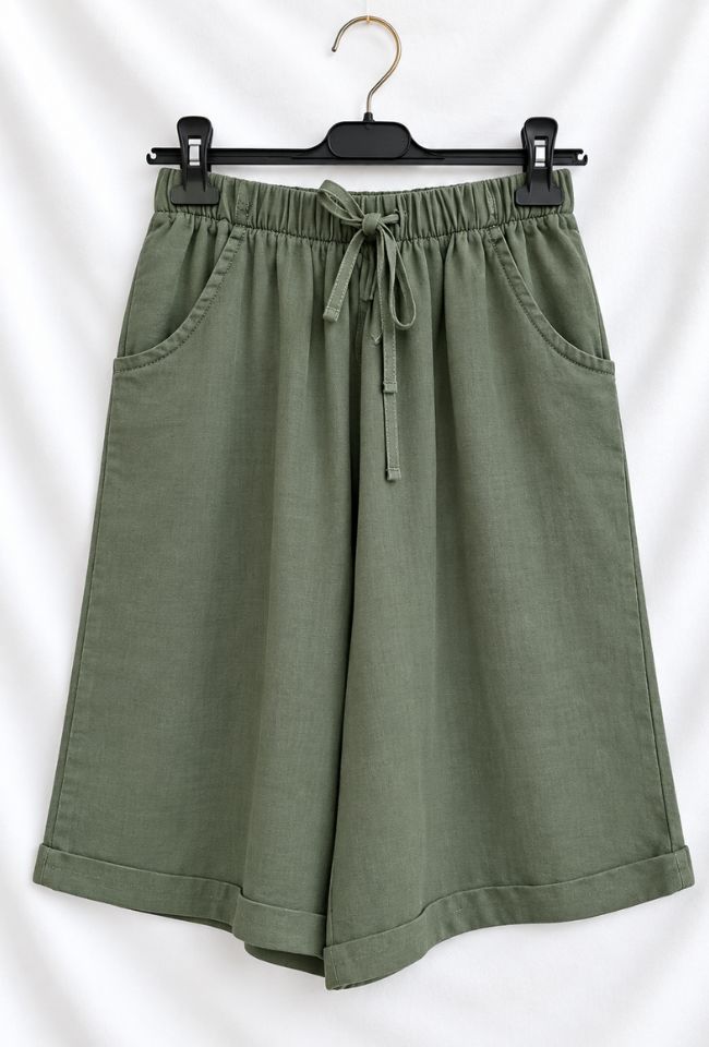 Olive green wide-leg shorts with an elastic drawstring waistband, displayed on a black hanger against a white fabric backdrop.
