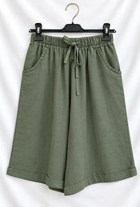 Olive green wide-leg shorts with an elastic drawstring waistband, displayed on a black hanger against a white fabric backdrop.
