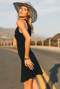 Woman in a black dress and straw hat standing on a road with mountains in the background