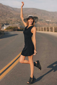 Woman in a black dress and hat standing on a road with mountains in the background