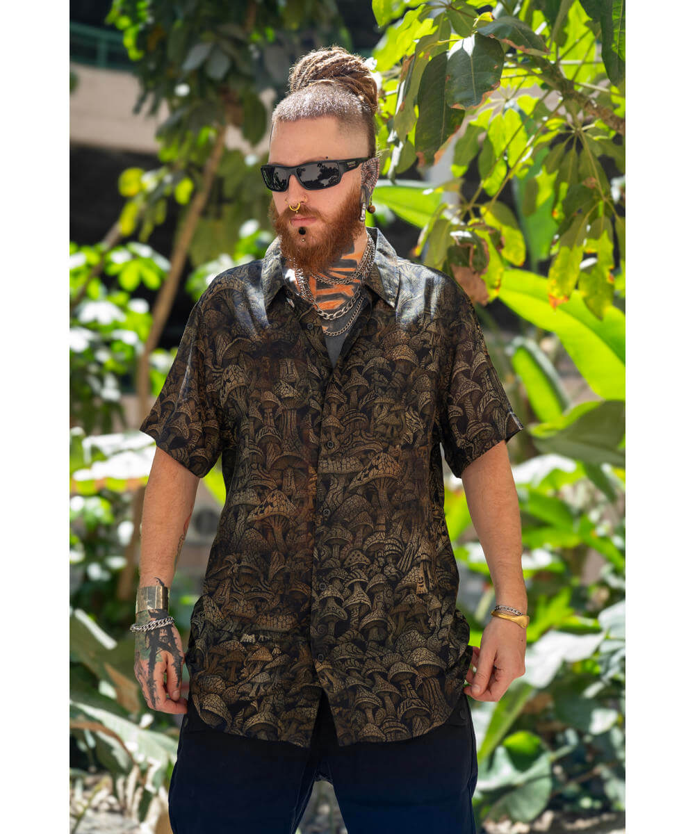 Man wearing a patterned shirt and sunglasses standing in front of green foliage