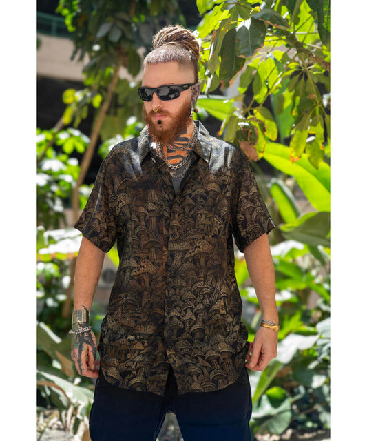 Man wearing a patterned shirt and sunglasses standing in front of green foliage