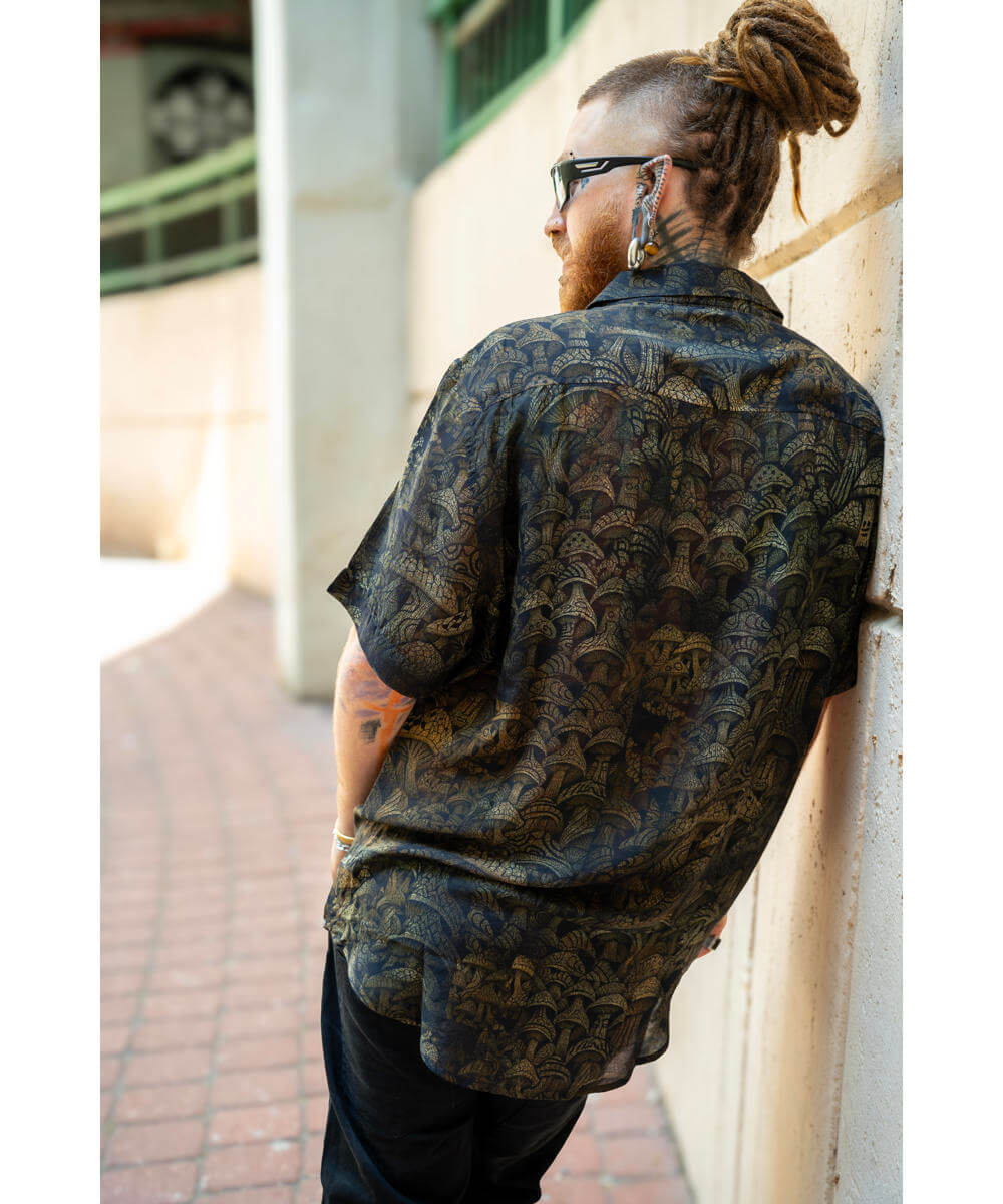 Man wearing a patterned shirt leaning against a wall outdoors