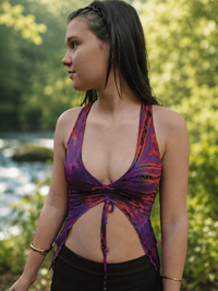Woman wearing a tie-dye top and black pants standing in a natural setting with trees and water.