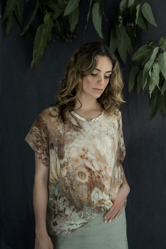 Woman wearing a patterned shirt against a dark background with greenery.