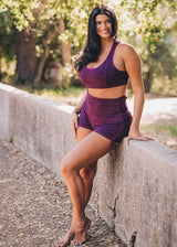 Woman in purple athletic wear leaning against a stone wall outdoors