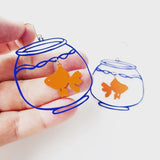 Goldfish bowl earrings with a hand holding one and a blue outline of a fishbowl on a white background.