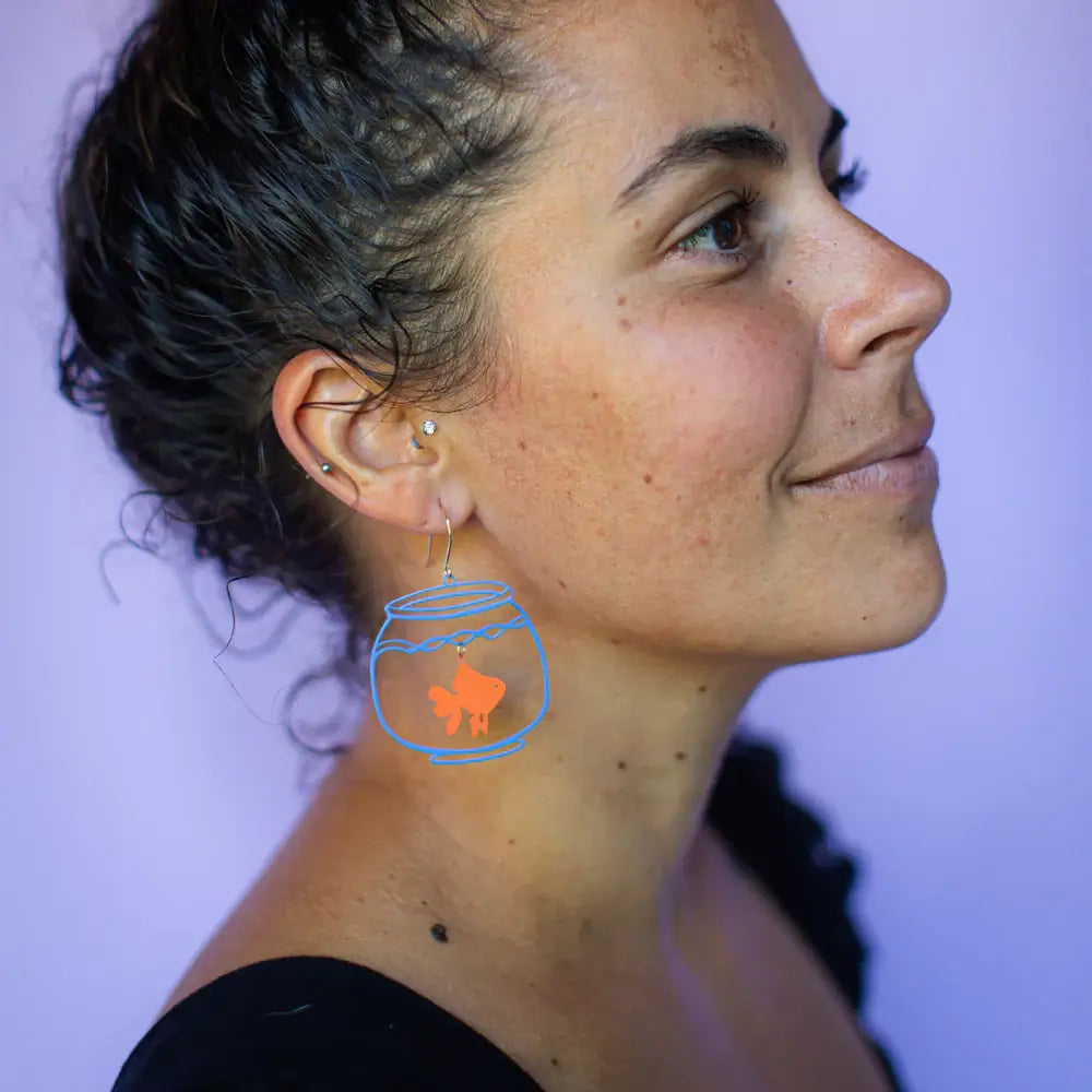 Close-up of a person wearing a fishbowl earring with a fish illustration.