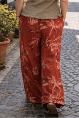 Woman walking down a street in an Italian town wearing a green sleeveless top and red floral pants.