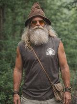 Man with long beard and hat wearing sunglasses, standing in a forest.