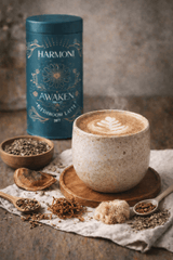 Cup of coffee with latte art on a wooden coaster, next to a blue canister labeled 'Harmoni Awaken'.