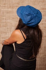 Woman wearing a blue beret sitting against a textured beige wall.