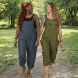 Two women walking outdoors in a park, wearing blue and green overalls.
