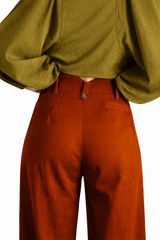 Person wearing a green top and rust-colored pants on a white background