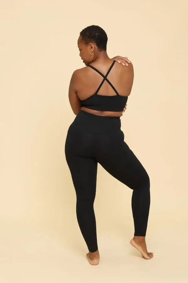 Person wearing a black sports bra and leggings set on a beige background