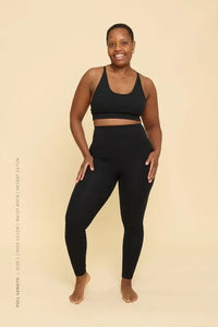 Woman wearing a black sports bra and leggings set on a beige background