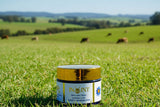 jar of INOINT tallow in a grass paddock with cows in the distance