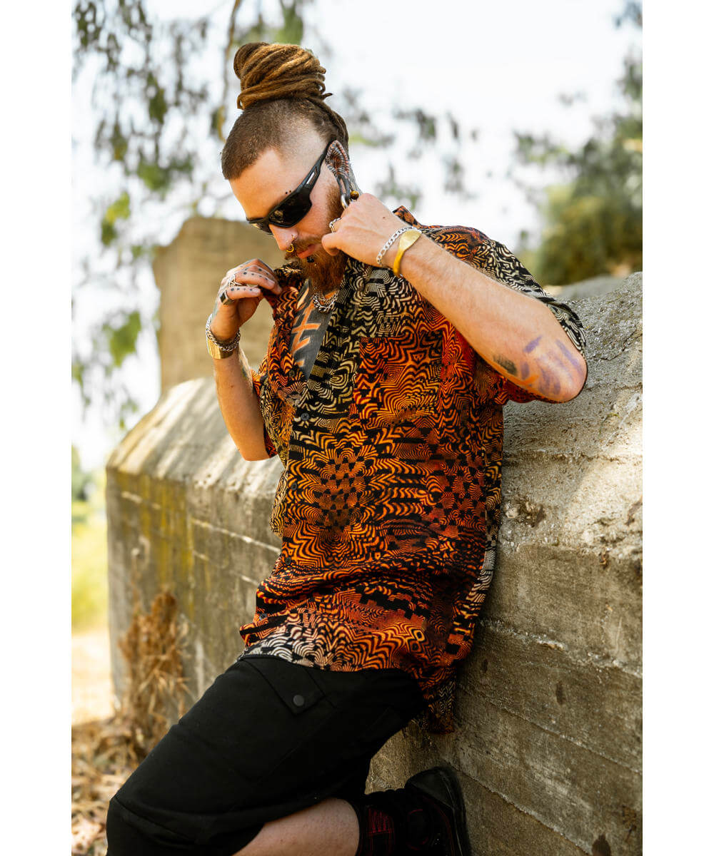 Man wearing a patterned shirt leaning against a stone wall outdoors