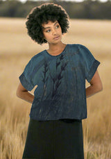 Woman wearing a blue patterned top and black pants on a white background