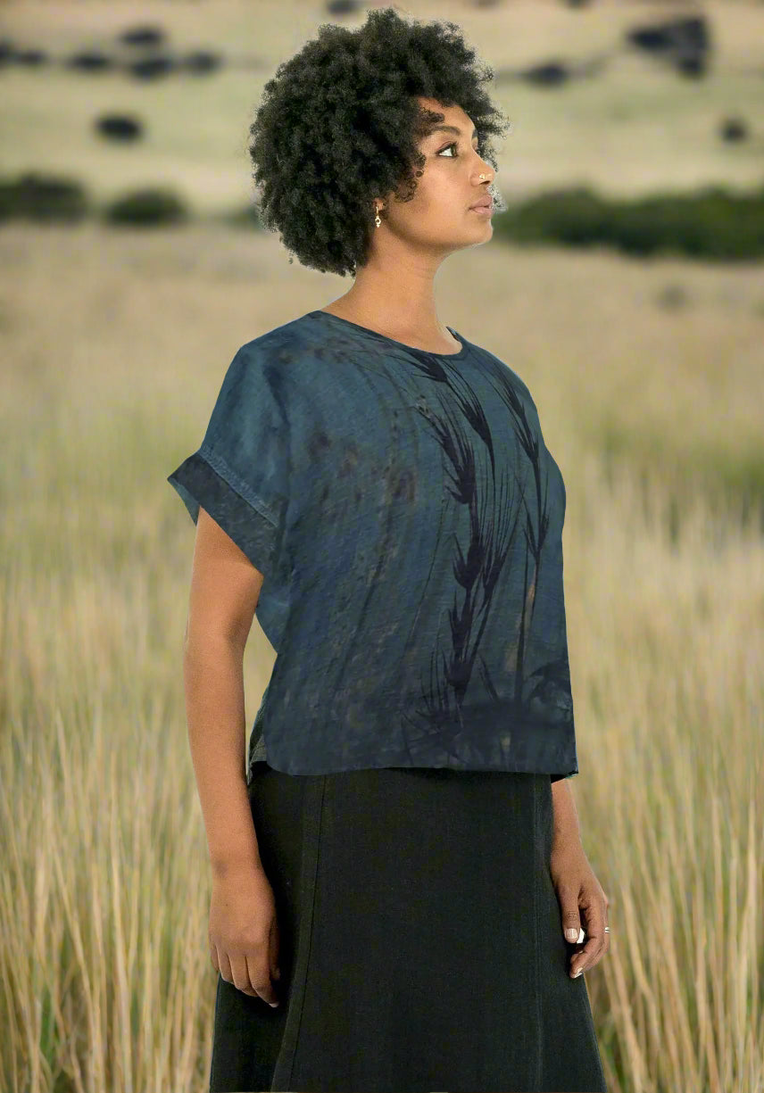 Woman wearing a blue tie-dye shirt and black pants with grass feild background
