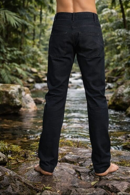 Person wearing black pants standing on rocks by a stream with a forest background