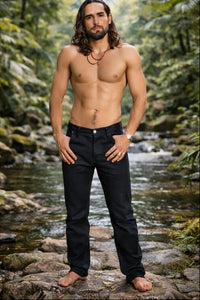 Man standing shirtless in a natural setting with a stream and greenery.