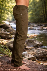 Person wearing green pants standing by a stream with trees in the background