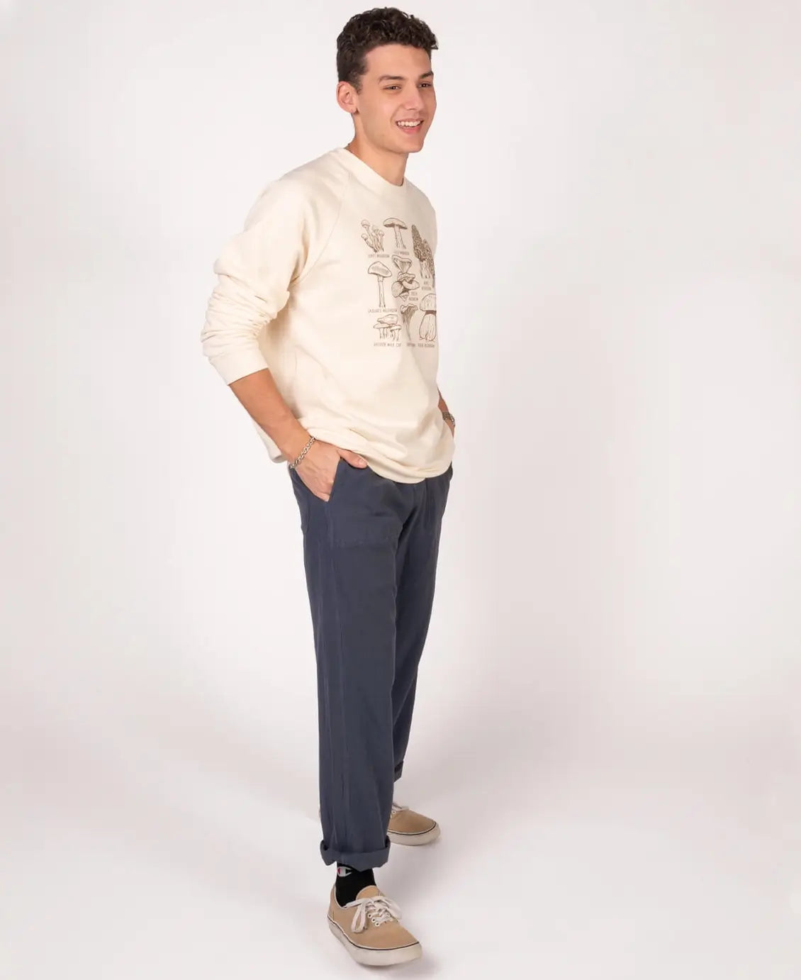 Man wearing a cream sweater and dark pants on a white background