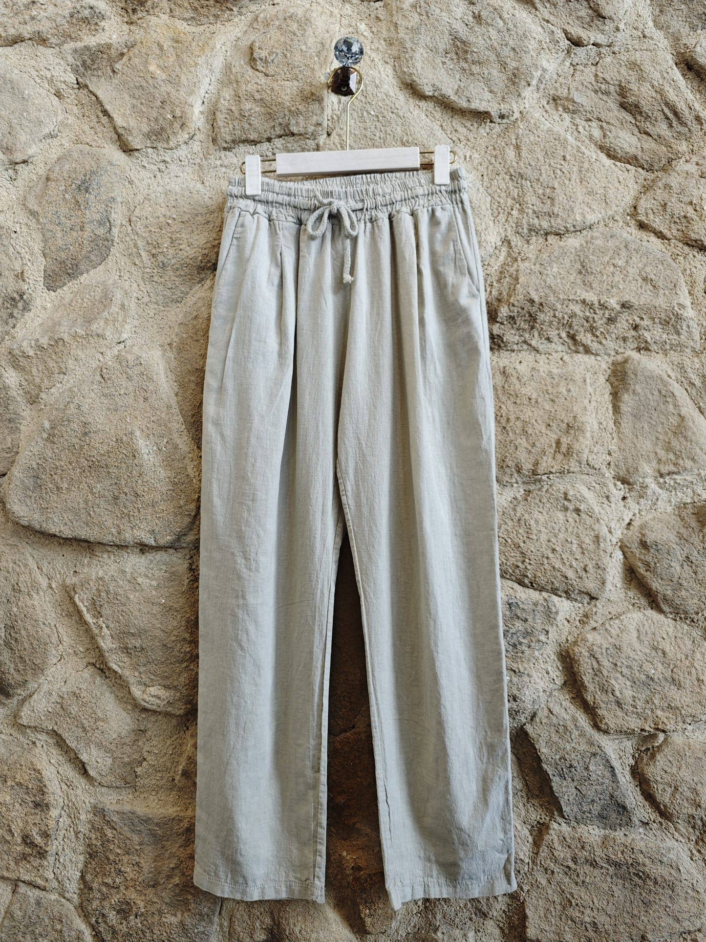 Light-colored pants hanging on a hook against a stone wall
