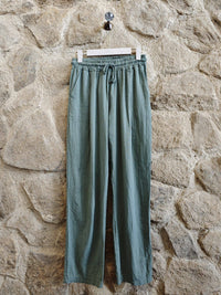 Green pants hanging on a hook against a stone wall