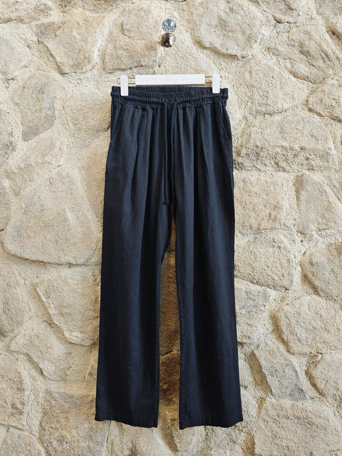 Black pants hanging on a hook against a stone wall