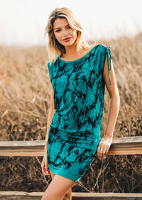 Woman wearing a teal dress with black patterns standing outdoors against a natural background.