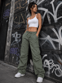 Woman in white crop top and green cargo pants leaning against a graffiti-covered wall.