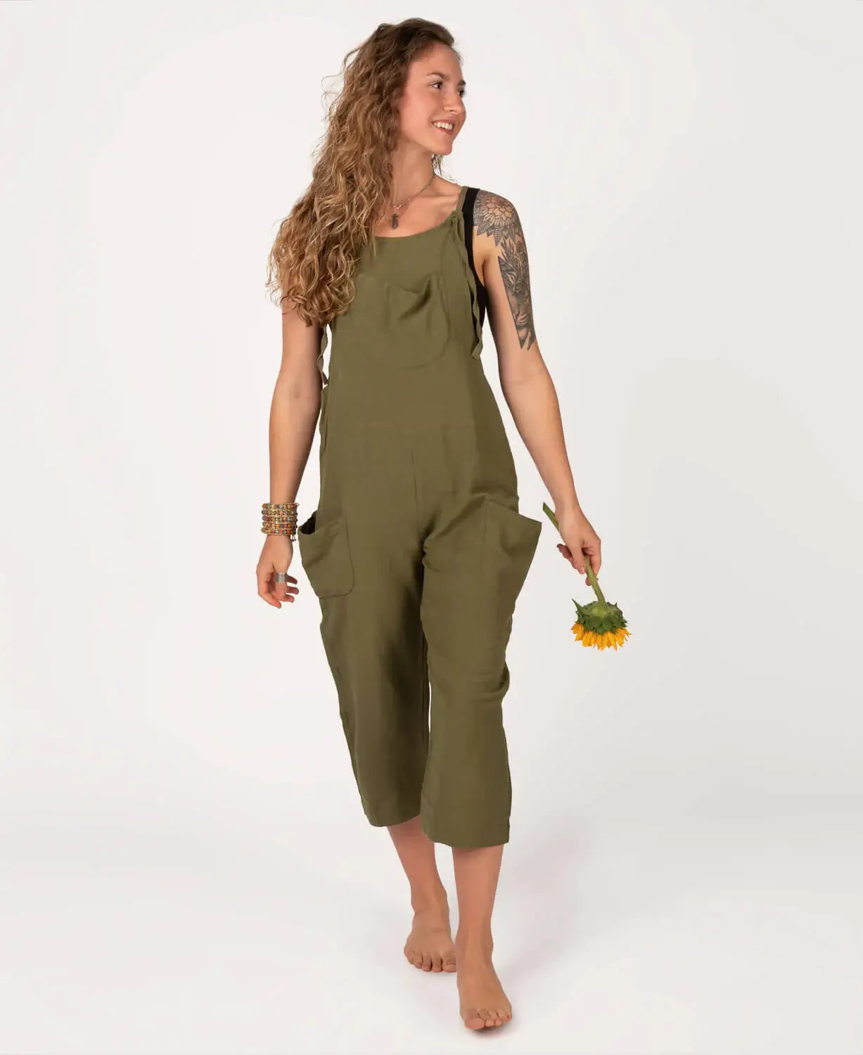 Woman wearing a green jumpsuit holding a small plant on a white background