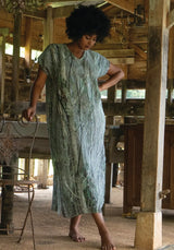 Woman in a light green dress standing in a rustic interior setting.