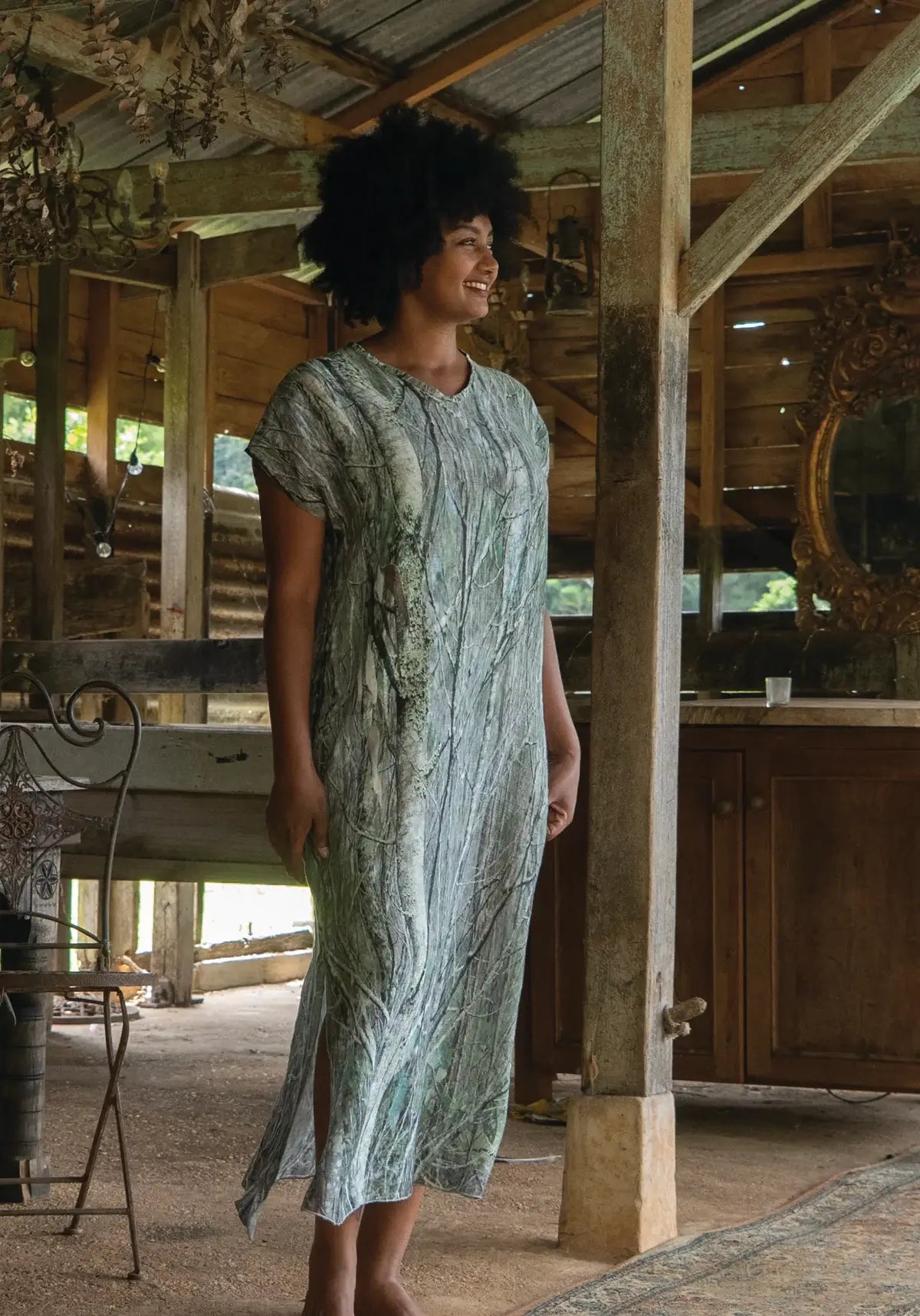 Woman in a patterned dress standing in a rustic wooden building.