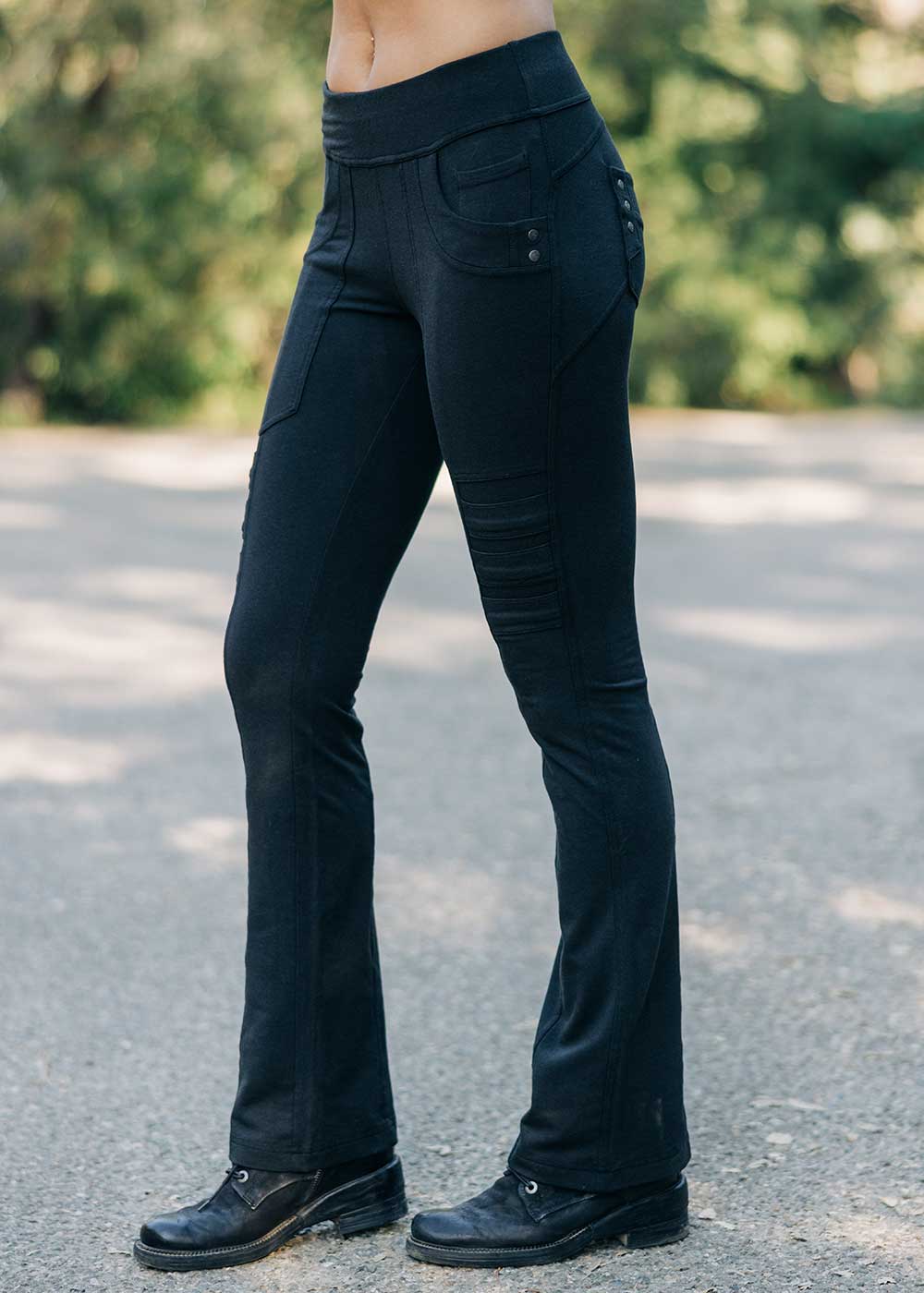 Person wearing black pants standing on a road with greenery in the background