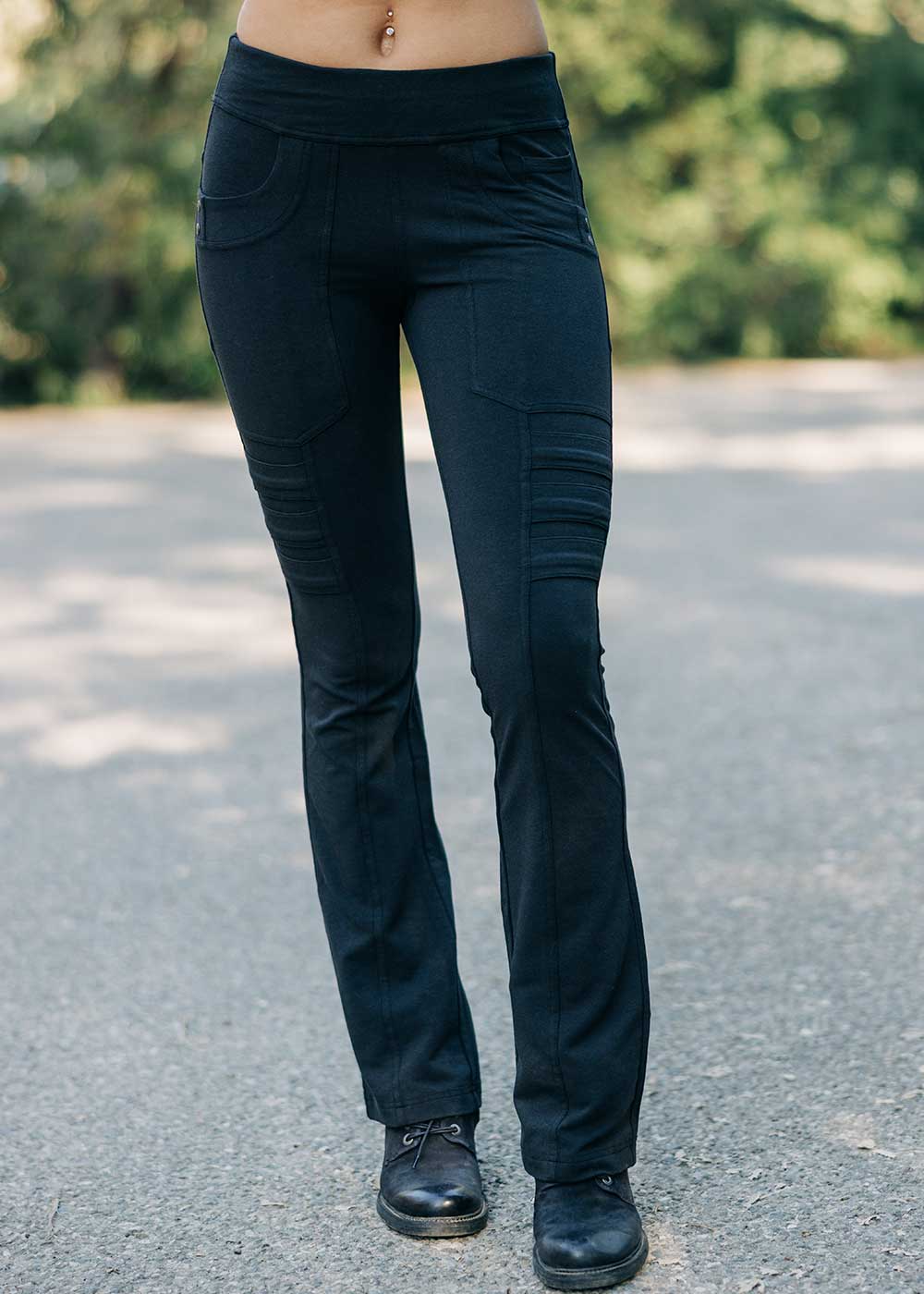 Person wearing black pants standing on a road with blurred greenery in the background