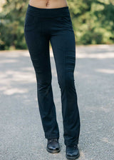 Person wearing black pants standing on a road with blurred greenery in the background