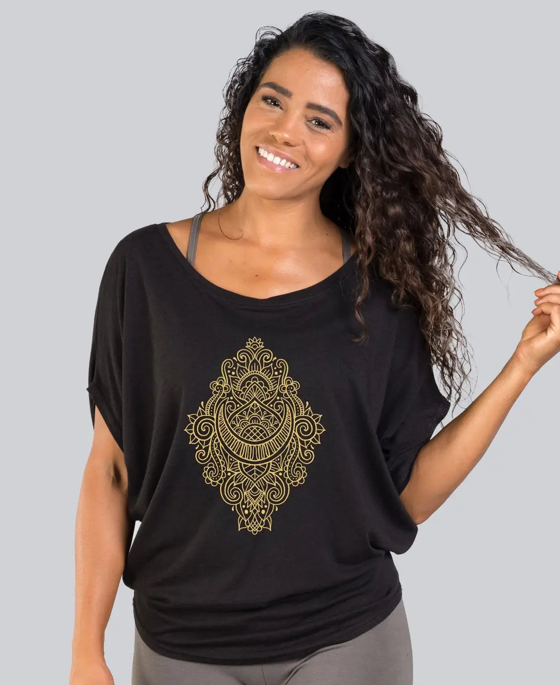 Woman wearing a black shirt with a gold mandala design on a gray background