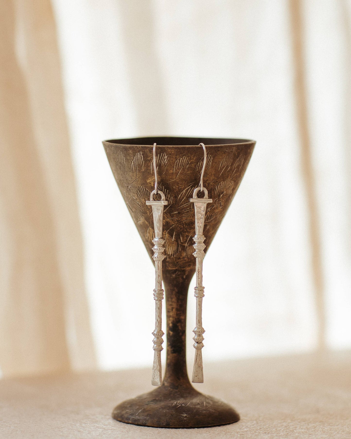 Nia Earrings long hammered white brass earrings displayed on a decorative stand