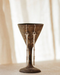 Nia Earrings long hammered white brass earrings displayed on a decorative stand