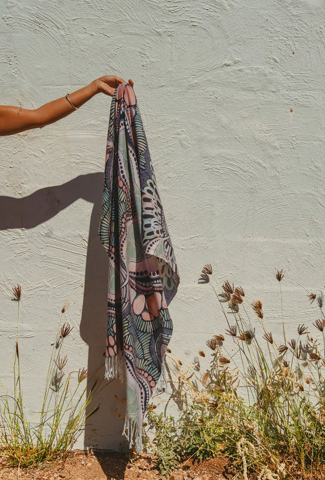 Place of Peace cotton beach towel draped over a timber railing, showcasing its detailed woven artwork and fringed edges