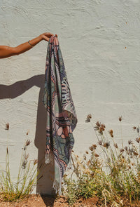Place of Peace cotton beach towel draped over a timber railing, showcasing its detailed woven artwork and fringed edges