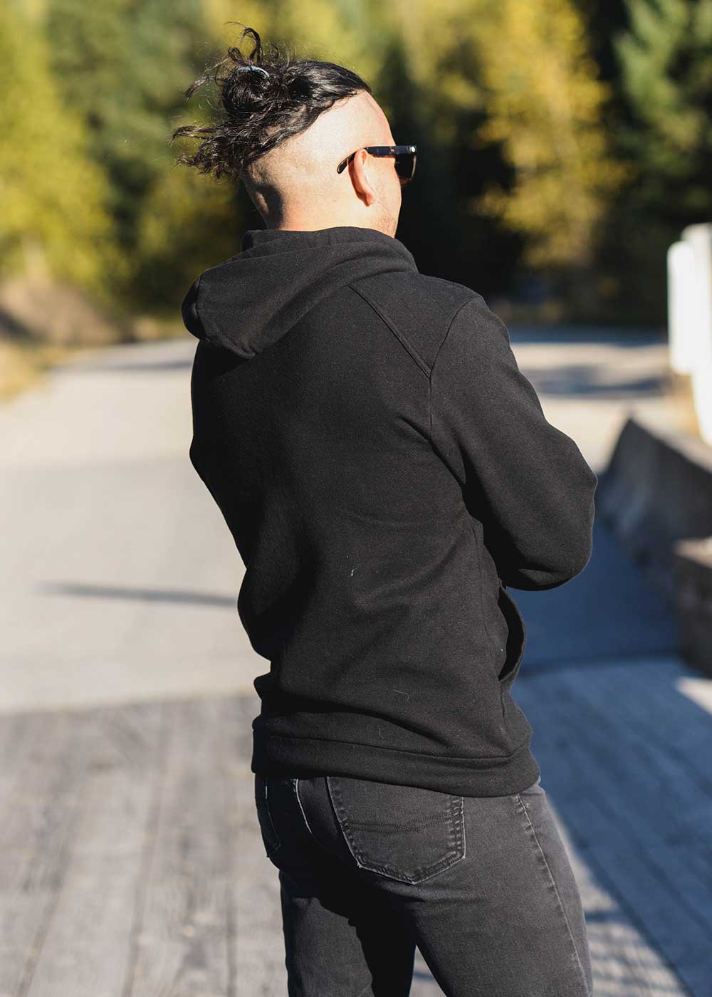 Person wearing a black hoodie and sunglasses, standing outdoors with trees in the background