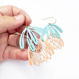 Hand holding a pair of colorful leaf-shaped earrings against a white background