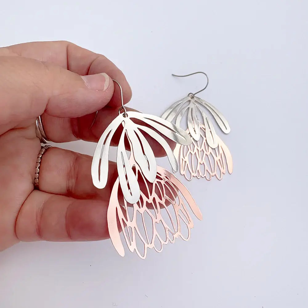 Hand holding a pair of silver and rose gold earrings against a light background