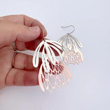 Hand holding a pair of silver and rose gold earrings against a light background