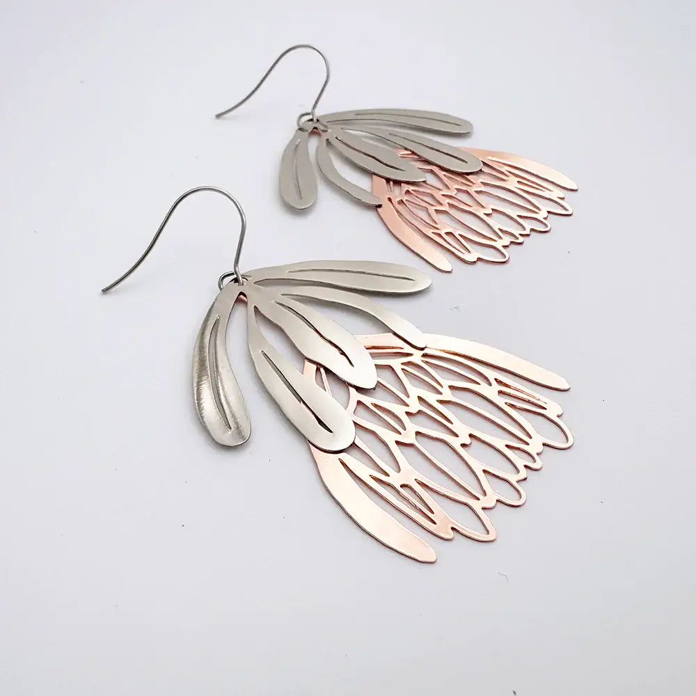 Pair of silver and rose gold leaf-shaped earrings on a light gray background